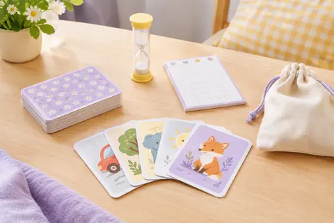 Cartes illustrées, sablier, carnet de score et sac présentés sur une table claire