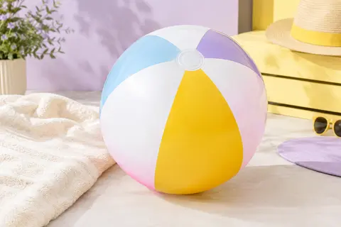 Ballon de plage gonflable multicolore de 61 cm posé dans un décor estival lilas et crème.