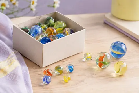 Billes en verre multicolores de deux tailles, présentées dans une boîte sobre sur un fond clair