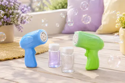 Deux pistolets à bulles en plastique bleu et vert avec leurs bouteilles de solution, posés dehors.