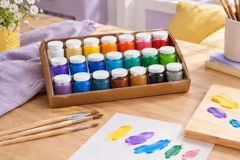 Kit de peinture acrylique aux couleurs vives avec trois pinceaux, présenté sur papier et bois clair.