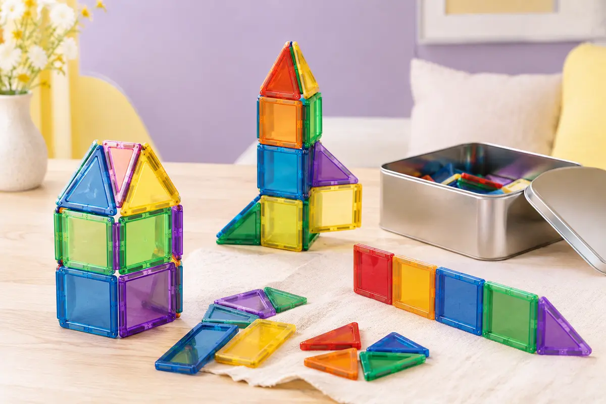 Tuiles magnétiques colorées assemblées près de leur boîte métallique sur un décor clair