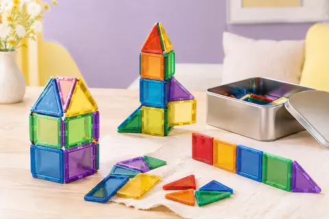 Tuiles magnétiques colorées assemblées près de leur boîte métallique sur un décor clair