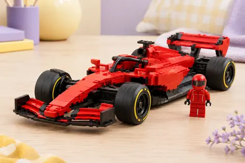 Voiture de F1 Ferrari SF-24 en briques rouges avec aileron arrière et pilote miniature sur fond clair.