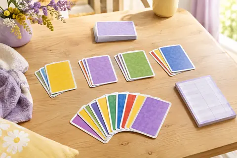 Cartes de jeu multicolores et bloc de scores disposés sur une table en bois clair