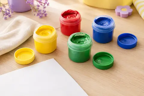 Quatre pots de peinture au doigt jaune, vert, rouge et bleu posés sur une table claire