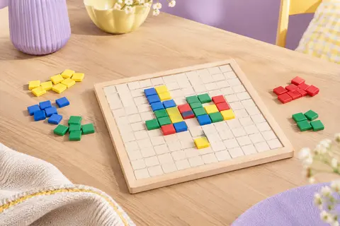 Plateau de jeu carré entouré de pièces multicolores en plastique sur une table claire