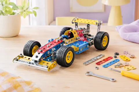 Véhicule de course en métal multicolore assemblé, présenté sur un décor clair aux accents lilas.