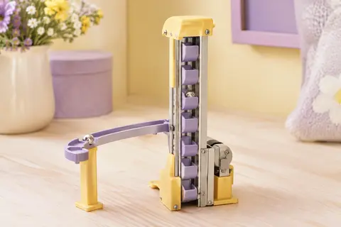 Élément ascenseur électronique pour circuit de billes posé sur une surface claire, avec une bille sur le parcours.