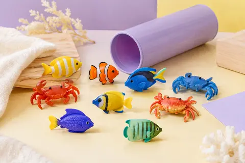 Tube de rangement entouré de mini-figurines multicolores représentant des poissons tropicaux et des crabes.