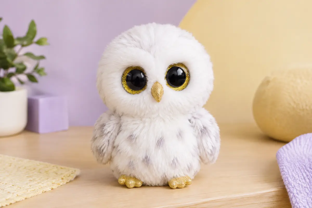 Peluche chouette blanche Austin de 15 cm, aux grands yeux brillants, posée sur un décor lilas et crème.